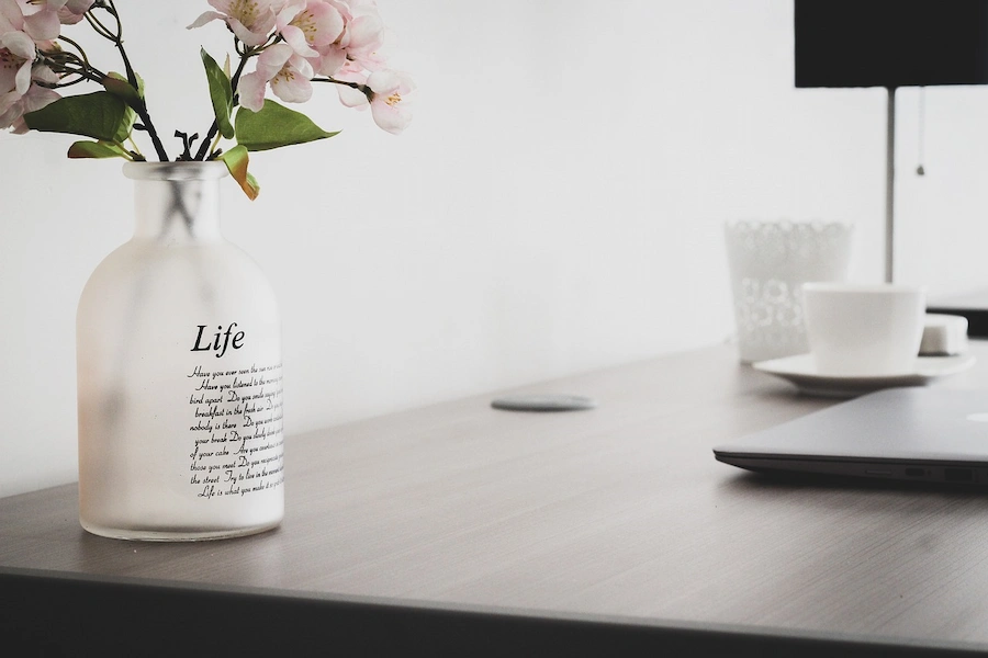 Secretária com um computador portátil e uma jarra com flores, com a palavra vida em inglês (Life)