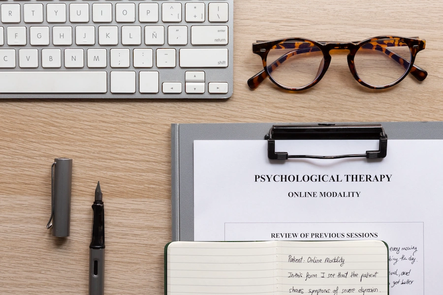 Mesa com teclado e apontamentos em papel de uma sessão de psicologia clínica online