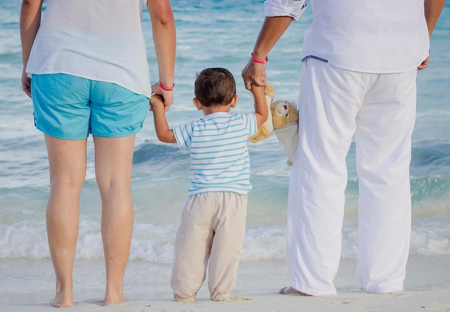 Pais de mão dada com criança à beira mar