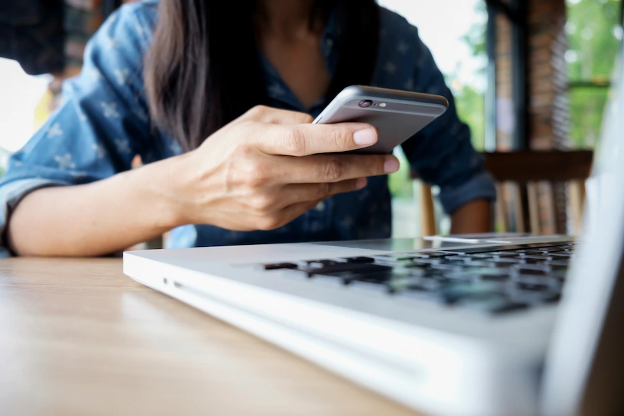 Pessoa a realizar pagamento online por telemóvel, sentada à mesa com um computador portátil à sua frente